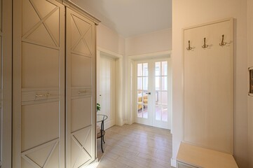 hallway with light beige walls, tiled floor, and a large wardrobe. There is a coat rack on the...