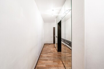 Long hallway with wood flooring, white walls, and a mirrored closet. Simple, clean interior design