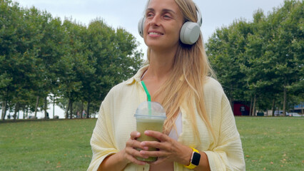 Woman Enjoying Green Smoothie and Music in Park by the Sea
