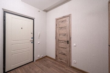 interior shot shows a hallway with two doors, one white with a black frame and the other a wooden color. The floor has wood grain planks