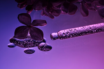 Cosmetic pipette with serum and lilac flowers on a purple background.