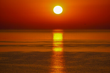 Sun setting over the sea at dusk with reddish tones