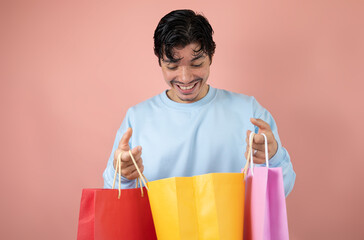 Happy man opening his yellow shopping bag on a pink background, shopping happiness concept