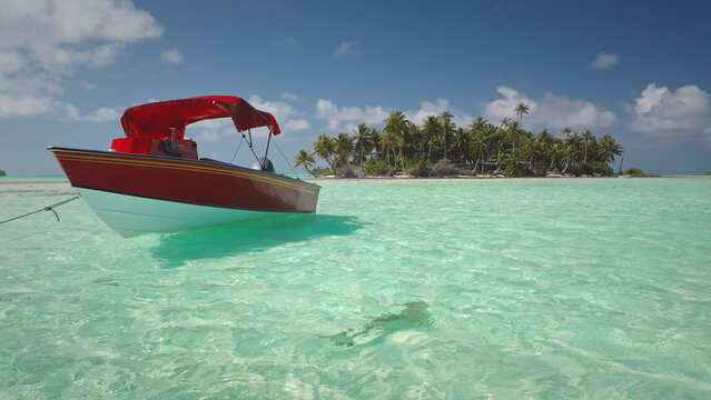 French Polynesia, Rangiroa island: Red and white boat with a bimini top mooring in shallow, crystal clear turquoise water near tropical island, Wild nature travel landscape. Drone flight