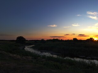 Serene stream in the countryside during sunset. Vibrant twilight colors reflect in calm water, natural beauty of rural evening.