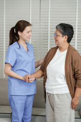 Obraz premium Senior asian woman standing with support from female asian physiotherapist while having conversation during physical therapy session in clinic focusing on elderly recovery