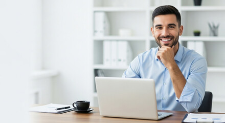 An approachable businessman sits confidently at his office desk with a laptop, embodying modern entrepreneurship and a successful career mindset