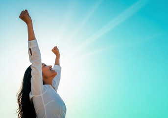 A triumphant woman raises her arms in celebration against a bright blue sky, symbolizing freedom, achievement, and reaching a personal peak