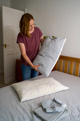Woman holding a pillow with fresh clean pillowcases, grey cotton bed sheets