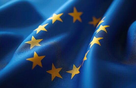 Close-up of European Union flag fabric, featuring circle of 12 yellow stars on blue background. Shows waving texture, symbolic unity of member states. Represents cooperation, democracy, international