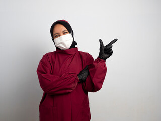 Young female nurse wearing a mask isolated on white background is surprised and pointing her finger...