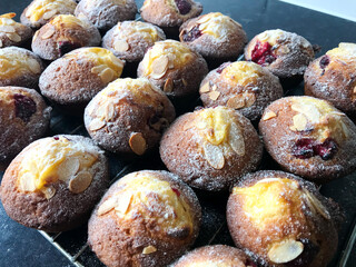 Close-up of a tray of freshly baked raspberry and almond muffins, golden brown and sprinkled with icing sugar on cooling rack, perfect for cozy kitchen scenes, baking themes, comforting food imagery
