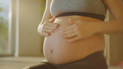 Pregnant woman applying cream for stretch marks on belly