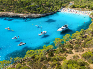 Aerial top view from drone of yachts and boats anchored in turquoise sea bay surrounded by rocky coastline and pine forest, summer vacation scene near Cala Mondrago, Mallorca, Balearic Islands, Spain