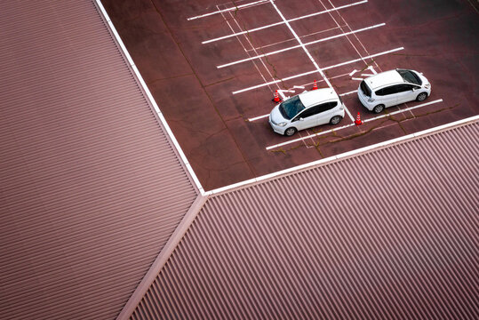 Aerial view of two white cars parked neatly in a parking spot next to the edge of a brown roof, Chikusei, Ibaraki, Japan.