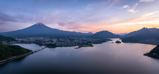 Aerial view of Mount Fuji looming majestically over the still, reflective waters of lake Kawaguchi, a bridge connecting the town to nature's embrace, Fujikawaguchiko, Yamanashi, Japan.