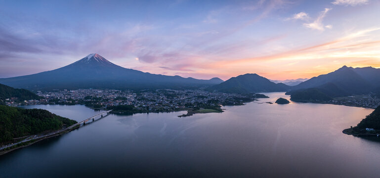 Aerial view of Mount Fuji looming majestically over the still, reflective waters of lake Kawaguchi, a bridge connecting the town to nature's embrace, Fujikawaguchiko, Yamanashi, Japan.