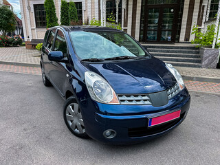 A stylish and compact blue hatchback is parked in an urban environment, showcasing its sleek design against a backdrop of modern architecture and vibrant city life, reflecting contemporary living