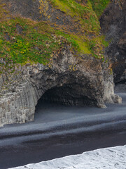 Coastal scene with basalt columns leading to a cave at Reynisfjara Beach. Dark volcanic sand...