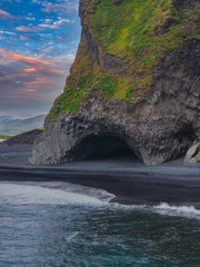 A coastal scene at Reynisfjara Beach, Iceland, featuring a moss covered basalt rock formation with...