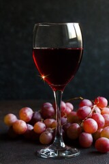 A glass of red wine is decorated with a branch of red fresh grapes on a black surface