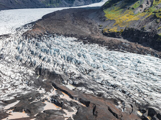 A glacier in Iceland flows through a valley, its icy surface streaked with volcanic ash. Steep...