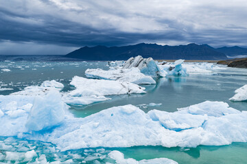 Jagged icebergs float in turquoise waters at Jokulsarlon Glacier Lagoon, framed by dark mountains...