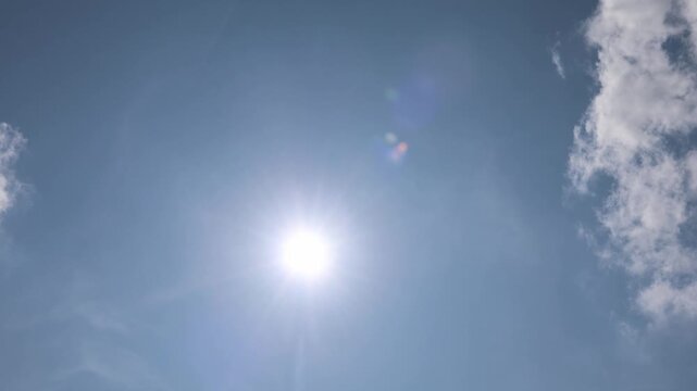 Bright sun shining with lens flare and few clouds passing by.