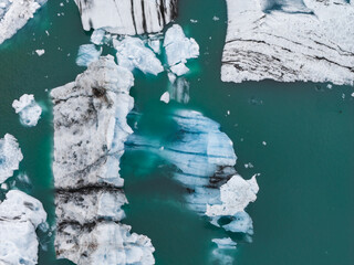 Large icebergs with black volcanic ash streaks and bright ice float in a turquoise glacial lagoon,...