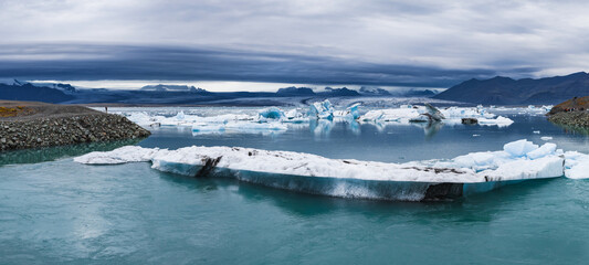 Turquoise waters of Jokulsarlon Glacier Lagoon with floating icebergs, a rocky shoreline, and...