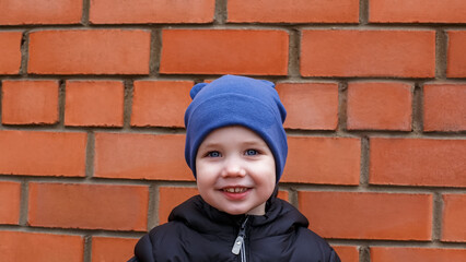 Portrait of a happy blue-eyed child against a brick wall.