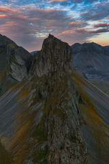 A dramatic mountain ridge with rocky slopes and moss, set against distant peaks and a colorful...