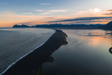 Aerial view of Iceland's Stokknes Peninsula at sunset, featuring a black sand beach, calm...