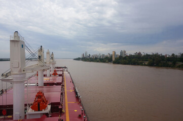 Сargo ship, bulk carrier with deck cranes, approaches city of Rosario, Rio Parana, Argentina.