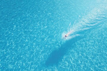 Fototapeta premium Calm water surface reflecting sunlight, swimmer creating ripples
