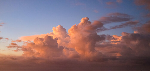 Towering clouds illuminated in warm orange and pink hues by the setting sun, standing against a soft gradient sky transitioning from blue to purple, creating a serene and dramatic evening atmosphere.