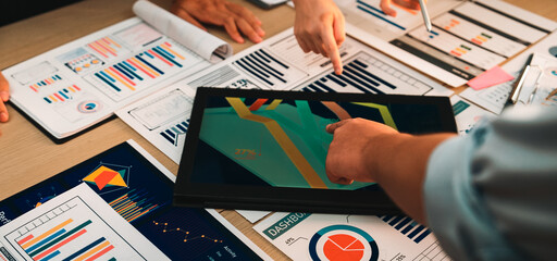 A diverse team collaborates in a modern office, engaging in data analysis. They use a digital tablet displaying colorful infographics while discussing charts and reports. SACTR