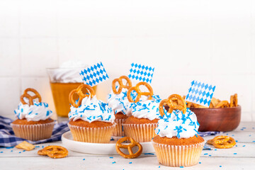 Oktoberfest cupcakes with salted pretzel, whipped cream on top and colorful sugar sprinkles, on white wooden background with Oktoberfest holiday decor, copy space