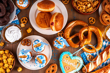 Oktoberfest festive food, with various snacks, sweets, desserts, pretzels, beer jelly, gingerbread cookies hearts, salted crackers, popcorn, jam donuts, cupcakes. Oktoberfest brunch menu background