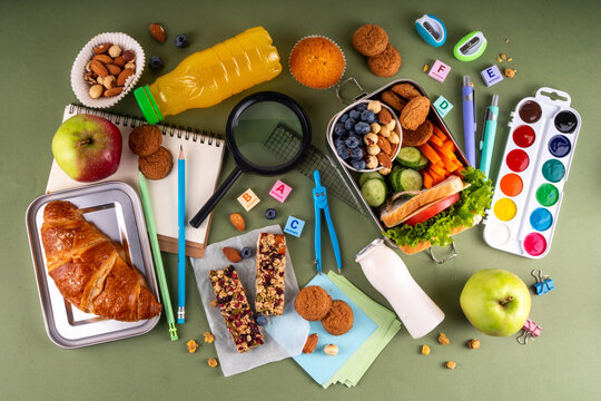 School healthy food for children. Preparing homemade balanced healthy lunch box for schooler, with sandwich, fruits, berries, juice, nuts. Ingredients and foods with school stationery and utensils