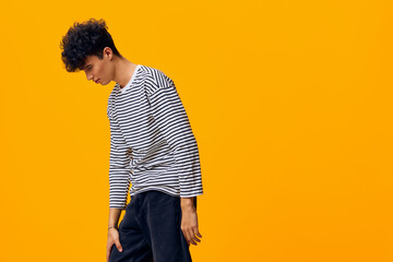 young man wearing striped shirt with curly hair posing thoughtfully on bright orange background,...