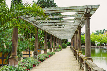 A serene garden pathway with a charming pergola, vibrant flowers, and a peaceful water body invites...