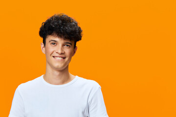 smiling man with curly hair wearing white t-shirt stands against bright orange background,...