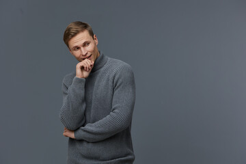 Smiling man, casual sweater, thoughtful mood, light brown hair, blue eyes, gray background, studio...