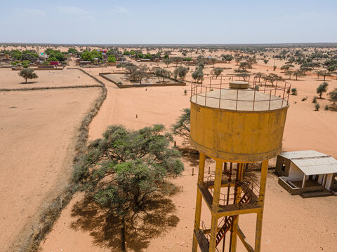 Aerial view of a yellow water tower stands tall against the arid landscape with sparse vegetation, Khol Khol, Louga Region, Senegal.