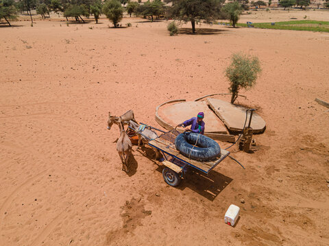 Aerial view of a man transporting a tire on a donkey-pulled cart near a unique structure in the arid landscape, Khol Khol, Louga Region, Senegal.