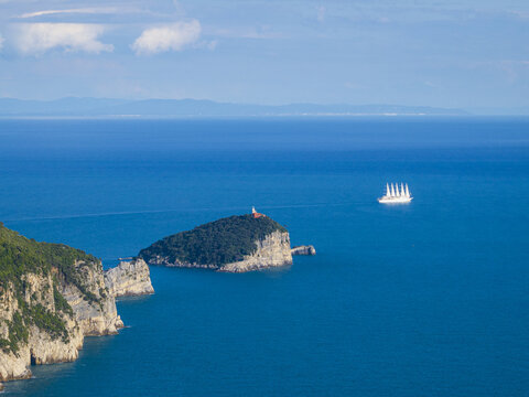 Aerial view of the deep blue sea surrounding the rugged coastline and the island of Tino with a lone sailing ship in the distance, Porto Venere, Liguria, Italy.