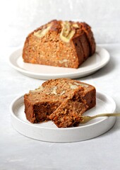 Homemade banana bread with carrot and walnuts on a white plate and white background