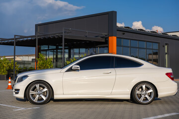 A beautifully designed sleek white luxury car is parked stylishly next to stunning modern architecture in the bright daylight, showcasing a perfect blend of elegance and contemporary aesthetics