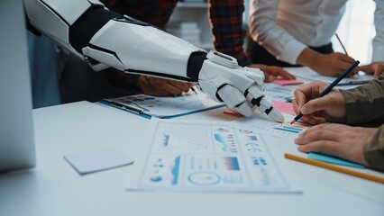 A futuristic scene depicting a robot arm collaborating with humans in an office. The team analyzes graphs and strategizes while utilizing modern tools and technology.Noogenesis
